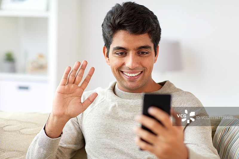 技术、人与沟通理念——快乐的男人与智能手机在家里视频通话。在家里用智能手机打视频电话的快乐男人图片素材
