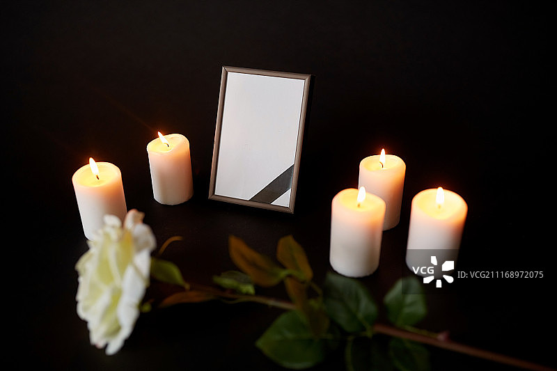 葬礼和悼念概念-相框黑色丝带，花和燃烧的蜡烛在黑暗中。配有黑丝带、鲜花和蜡烛的相框图片素材