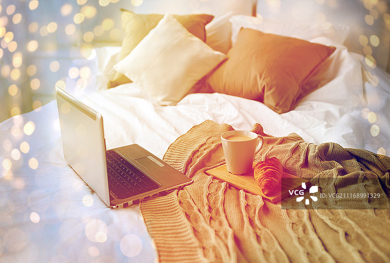 舒适，科技，室内和冬季概念-舒适的卧室与笔记本电脑，咖啡杯和羊角面包在床上在家。笔记本电脑，咖啡和羊角面包，躺在舒适的家里的床上图片素材