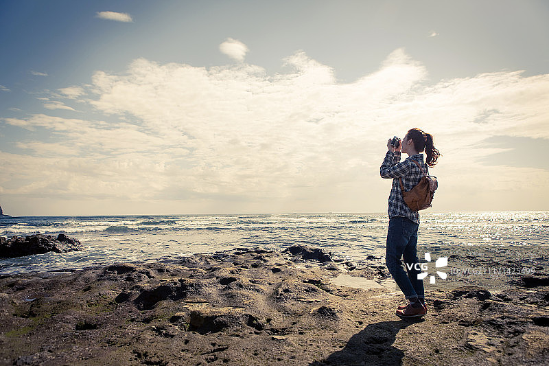 摄影的女人背着背包在海滩上用相机拍照图片素材