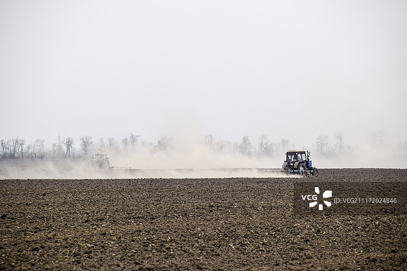拖拉机耙着地里的土壤，在后面扬起一团尘土图片素材