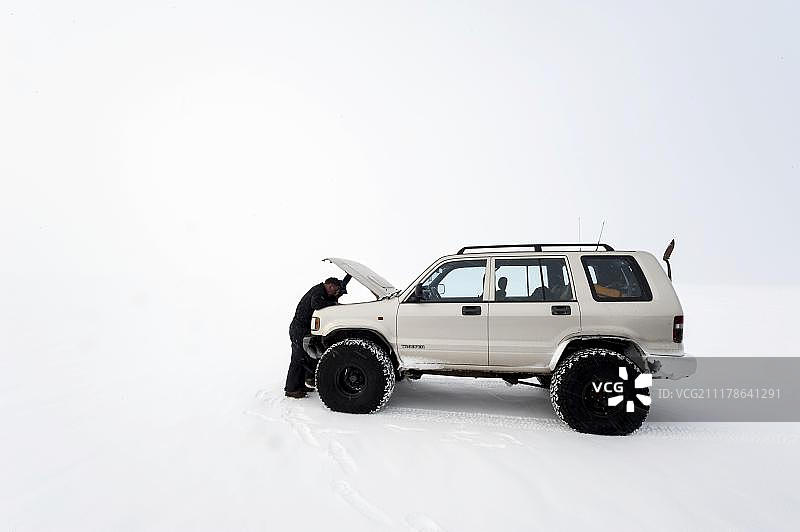 欧洲，冰岛高地，Vatnajoekull冰川，一名男子在冬季修理一辆超级吉普车时，打开发动机罩看发动机室图片素材