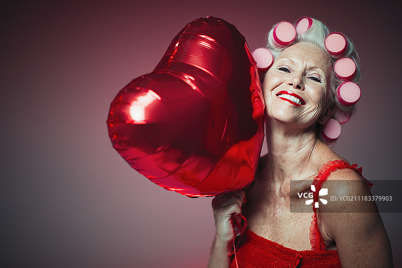 肖像俏皮的老妇人的卷发器拿着心形的气球图片素材
