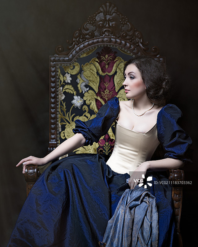 年轻优雅的女子坐在装饰扶手椅上，穿着长连衣裙和蓬松的袖子拿着围巾图片素材