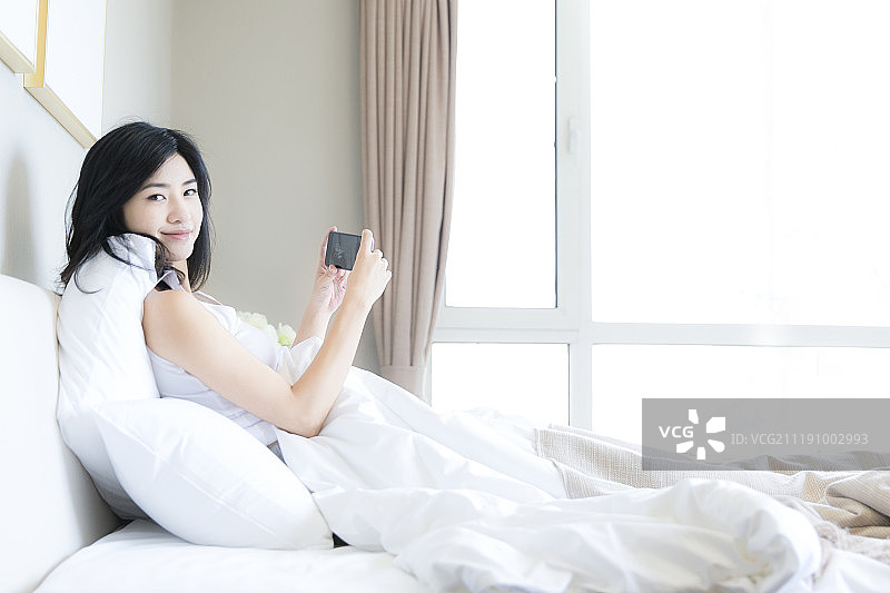 年轻女子在卧室床上用手机图片素材