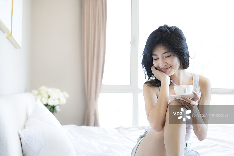 年轻女子坐在卧室床上喝咖啡图片素材