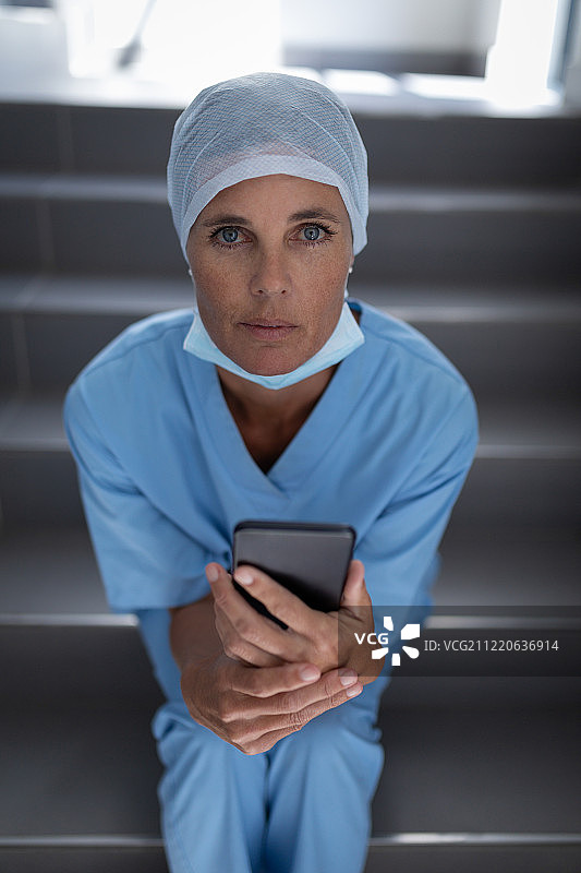 一位白种女外科医生坐在楼梯上拿着手机，看着镜头的肖像图片素材