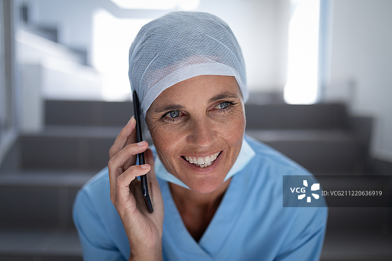 正面的一个白人女外科医生微笑和打电话，而坐在医院的楼梯情况图片素材