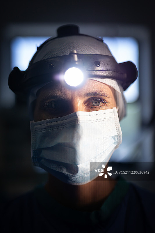 一个成熟的白种女外科医生在医院里用外科头灯看着摄像机的正面视图。图片素材