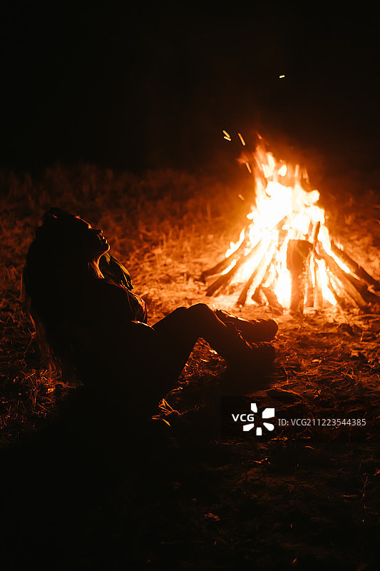 在暗夜森林里，一个女人坐在篝火旁取暖图片素材