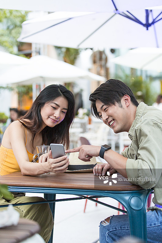 甜蜜情侣在露天咖啡馆旅游休息看手机图片素材