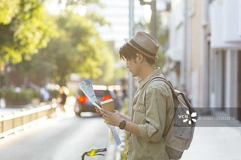 青年男子拿着咖啡看着旅游路线图在户外旅行度假图片素材