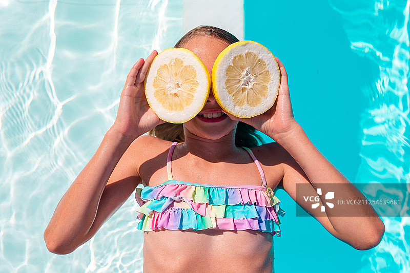 小女孩用柠檬盖住眼睛近旁的背景游泳池图片素材
