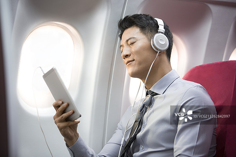 成功男商务人士在飞机上拿着平板电脑带着耳机听音乐图片素材
