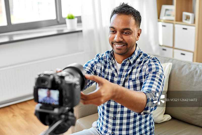 博客，视频博客和人的概念-微笑的印度男性视频博客调整相机在家。印度男性视频博主在家调整相机图片素材