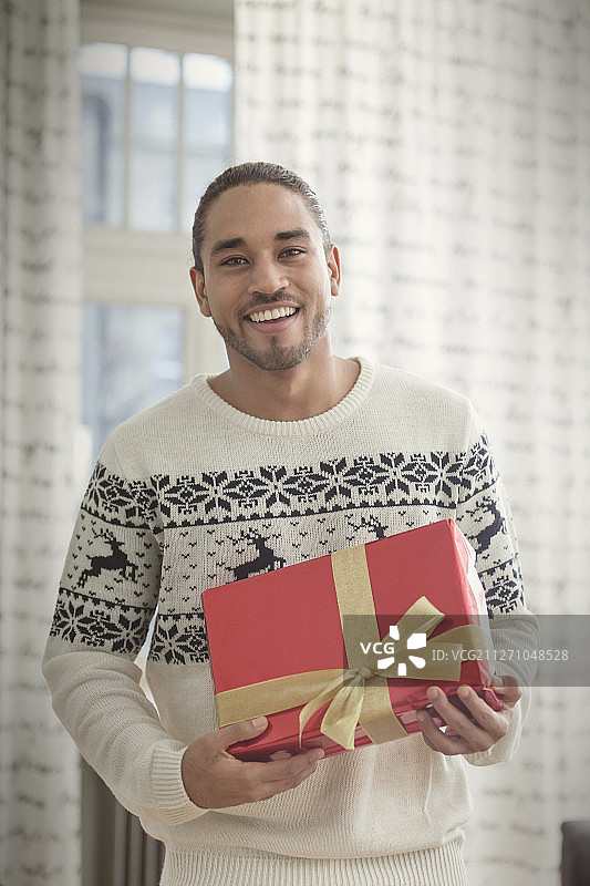 肖像微笑的年轻人在圣诞毛衣拿着礼物图片素材