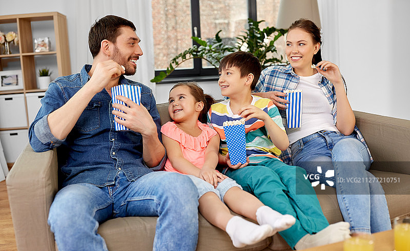 家庭、休闲和人的概念——快乐的母亲、父亲、儿子和女儿在家里看电视爆米花。幸福的家庭和爆米花在家里看电视图片素材