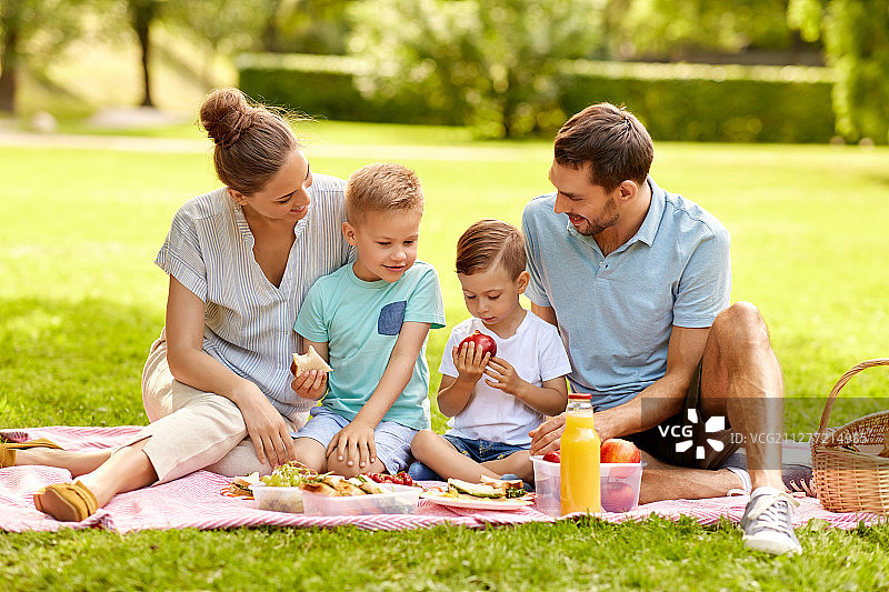 家庭、休闲、人的概念——快乐的妈妈、爸爸和两个小儿子在夏日公园野餐。快乐的家庭在夏季公园野餐图片素材