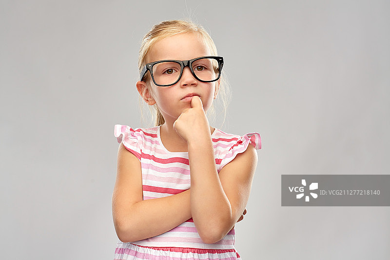 教育，学校和视觉概念-可爱的小女孩在黑色的眼镜在灰色的背景。可爱的小女孩戴着黑眼镜思考图片素材