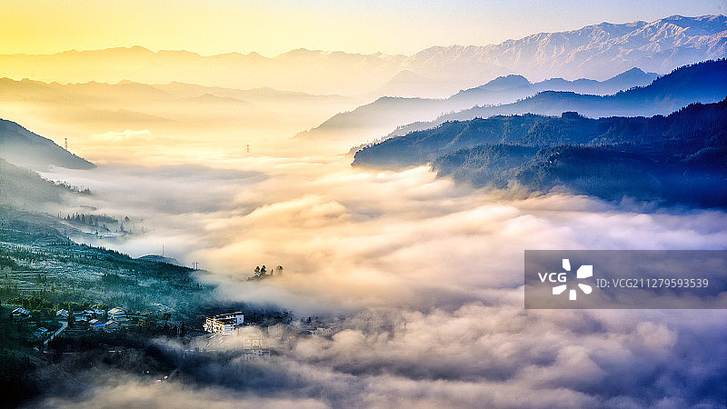 起伏绵延的山峦形成的山谷中被晨光照亮的流动云雾笼罩着山里人家图片素材
