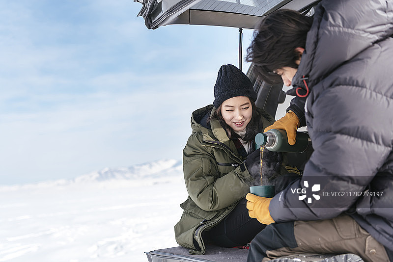 这是一对夫妇坐在汽车后备箱上，在雪地里喝咖啡的照片图片素材