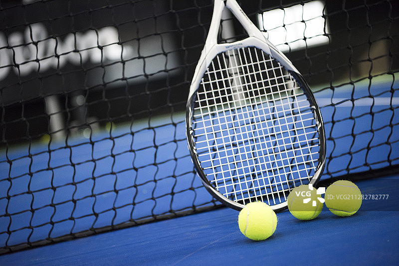 拍摄室内场地上的三个网球和球网旁边的球拍图片素材