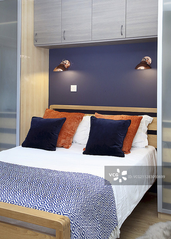 双人床，紫色墙壁上有台灯和壁挂式橱柜图片素材