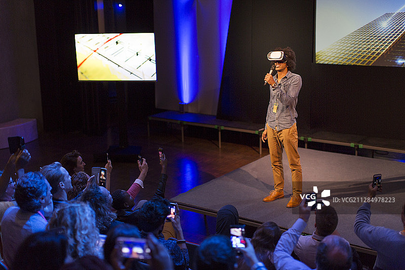 观众在台上观看戴着虚拟现实模拟器眼镜的男性演讲者图片素材