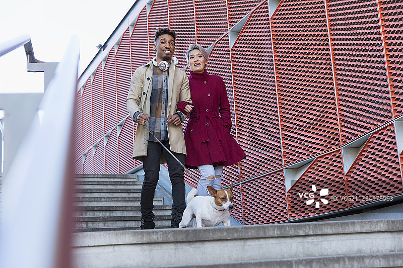 微笑的年轻夫妇遛着狗走下现代化的城市楼梯图片素材