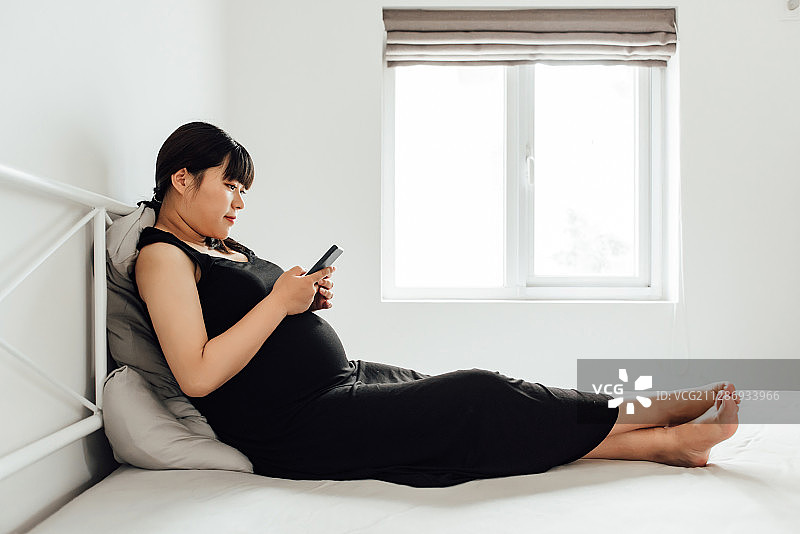 一位年轻的亚洲孕妇正在使用电子设备图片素材