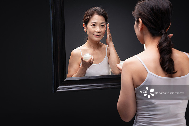 对着镜子涂抹护肤品的优雅女人图片素材