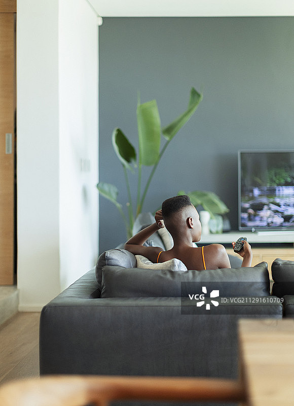 年轻女子拿着遥控器在客厅的沙发上看电视图片素材