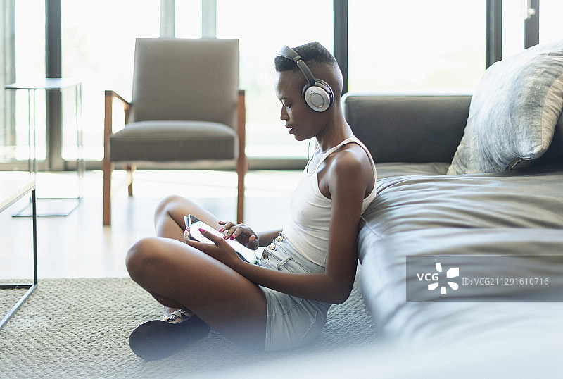 年轻女子在客厅里用耳机和平板电脑听音乐图片素材