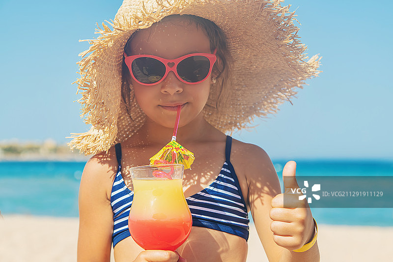 沙滩上的女孩喝着五颜六色的饮料，竖起大拇指图片素材