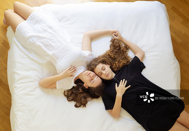 意大利卡利亚里，年轻的姐妹们躺在家里的床上图片素材