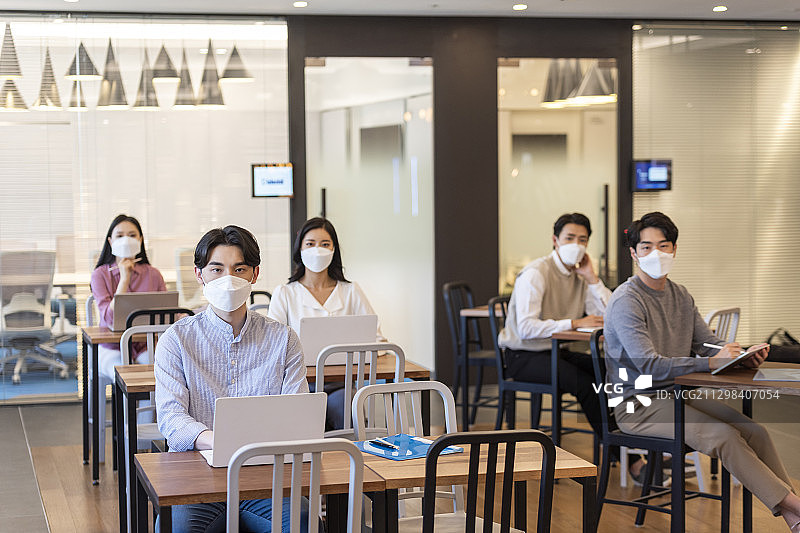 带着污染口罩的商人和女商人分别坐在不同的桌子旁，用笔记本电脑工作图片素材