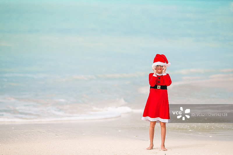 可爱的女孩戴着圣诞老人帽，站在海滩上图片素材