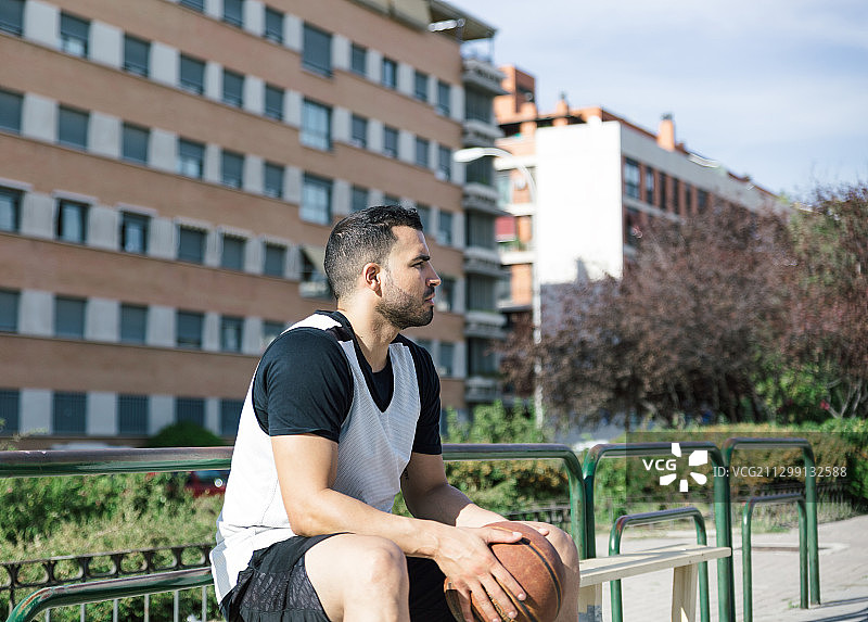 一个篮球运动员坐在他的手里拿着篮球准备出去打在一个城市的球场，马德里，西班牙图片素材