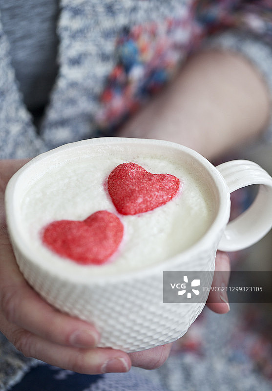 一个女人，手里拿着一杯热巧克力，上面有鲜奶油和粉红色的心形棉花糖图片素材