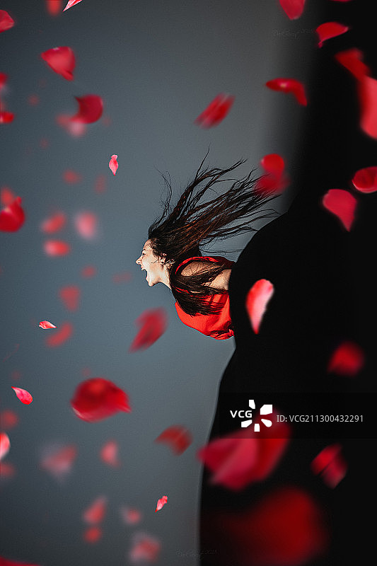 在黑暗的背景下，穿着红色连衣裙和玫瑰花瓣的女人图片素材