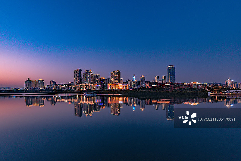蓝调时刻的城市夜景，建筑的灯光倒映在蓝色的湖水中图片素材
