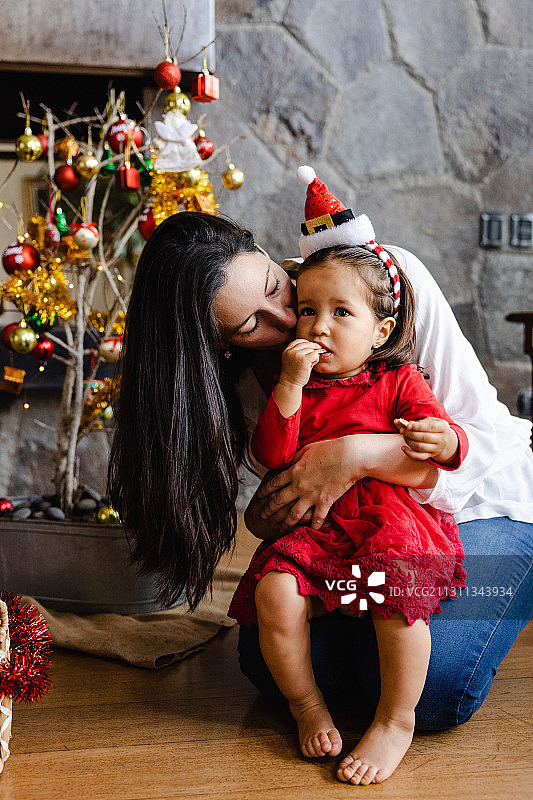 秘鲁利马，母亲坐在家里圣诞树旁亲吻女儿图片素材