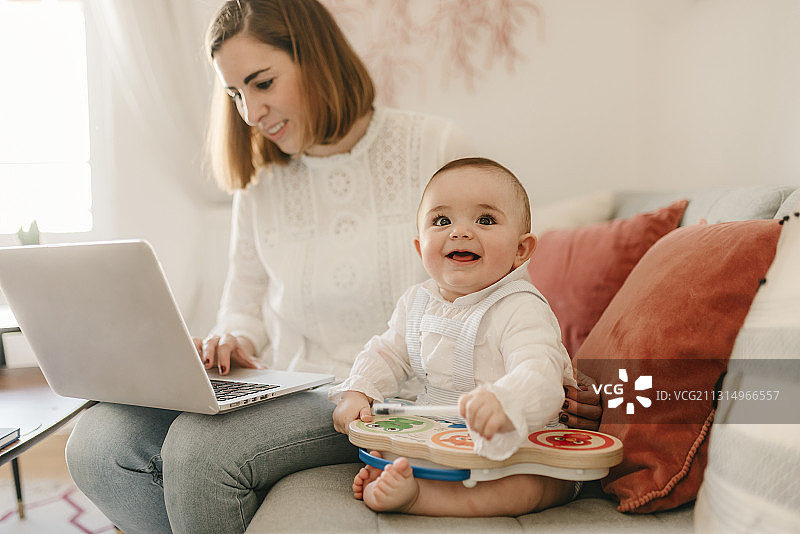 西班牙，母亲和男婴坐在家里，使用笔记本电脑图片素材
