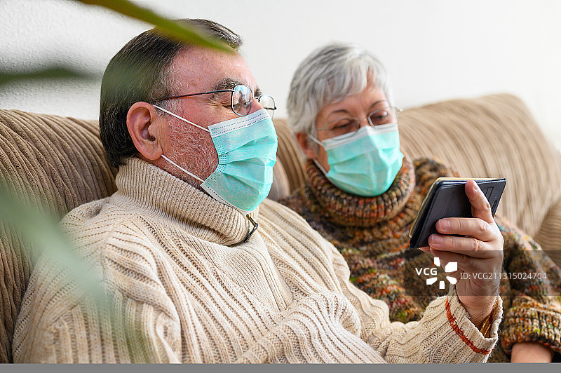 在家里戴着医用口罩使用手机的老年男女图片素材