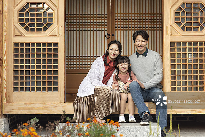 一家人微笑地坐在传统韩国房子的木地板上图片素材