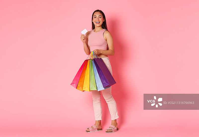 微笑的女人拿着购物袋的肖像，而站在粉红色的背景图片素材