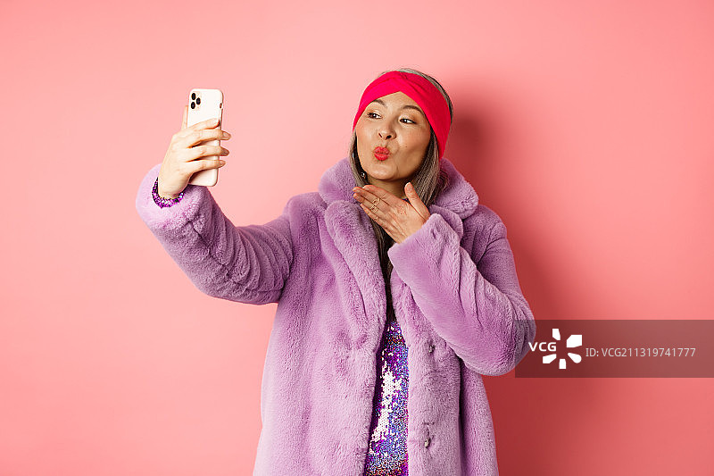 一名女子站在粉色背景下玩手机图片素材