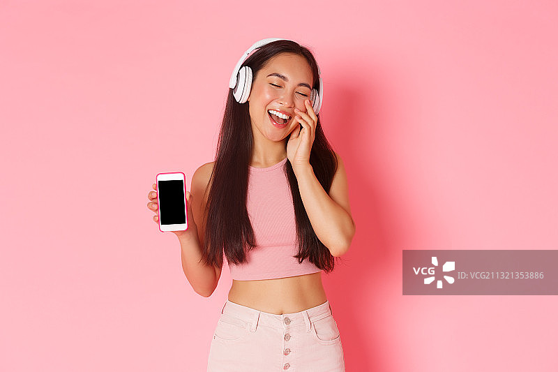 微笑的女人一边听音乐一边用手机做粉色的背景图片素材