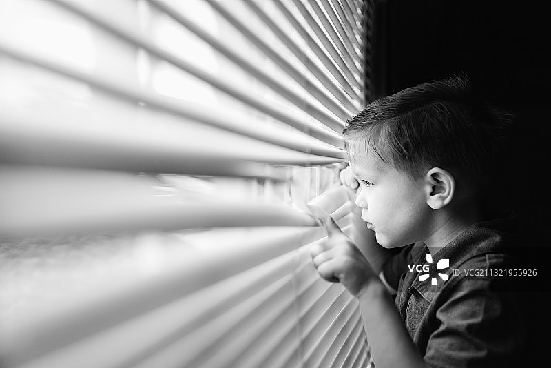 男孩从家里的百叶窗往外看图片素材
