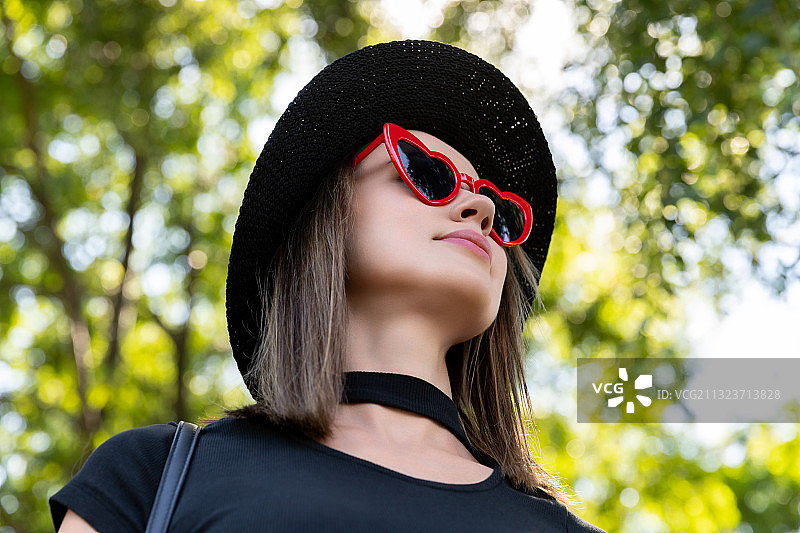 女人戴着心形太阳镜和帽子靠在树上图片素材